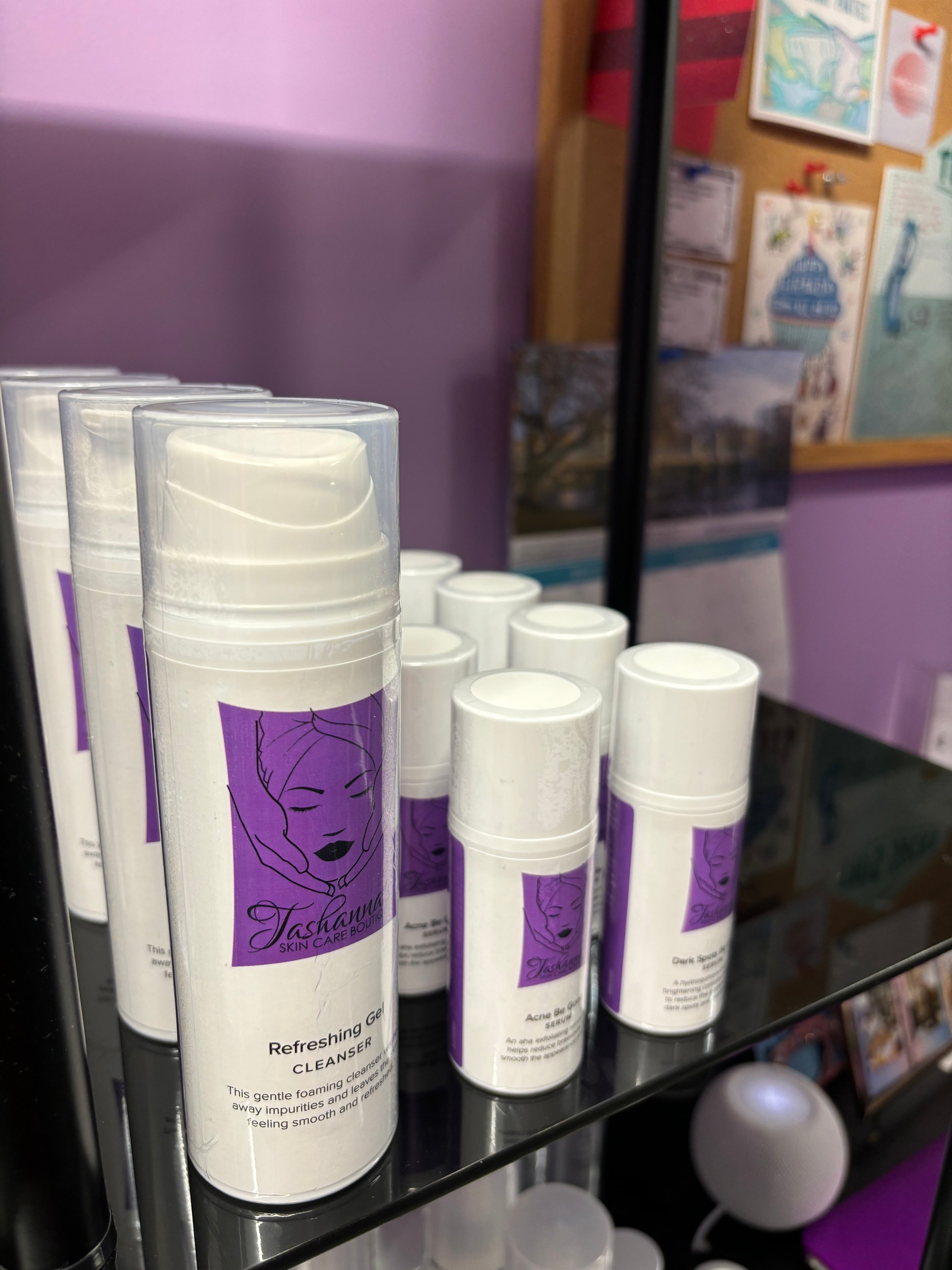 White skincare bottles with purple labels on a shelf against a purple wall.